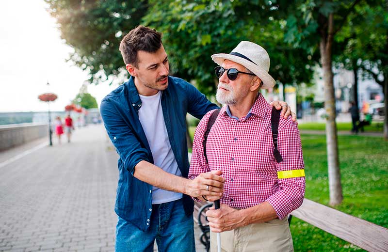 Un auxiliaire de vie sociale accompagne une personne aveugle dans un parc