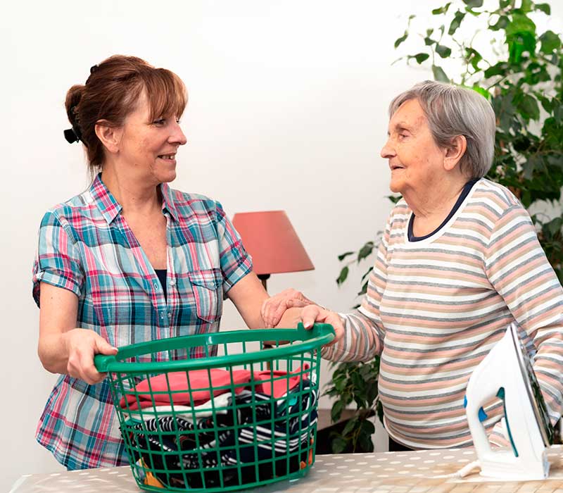 Une aide à domicile aide une personne âgée pour repasser le linge