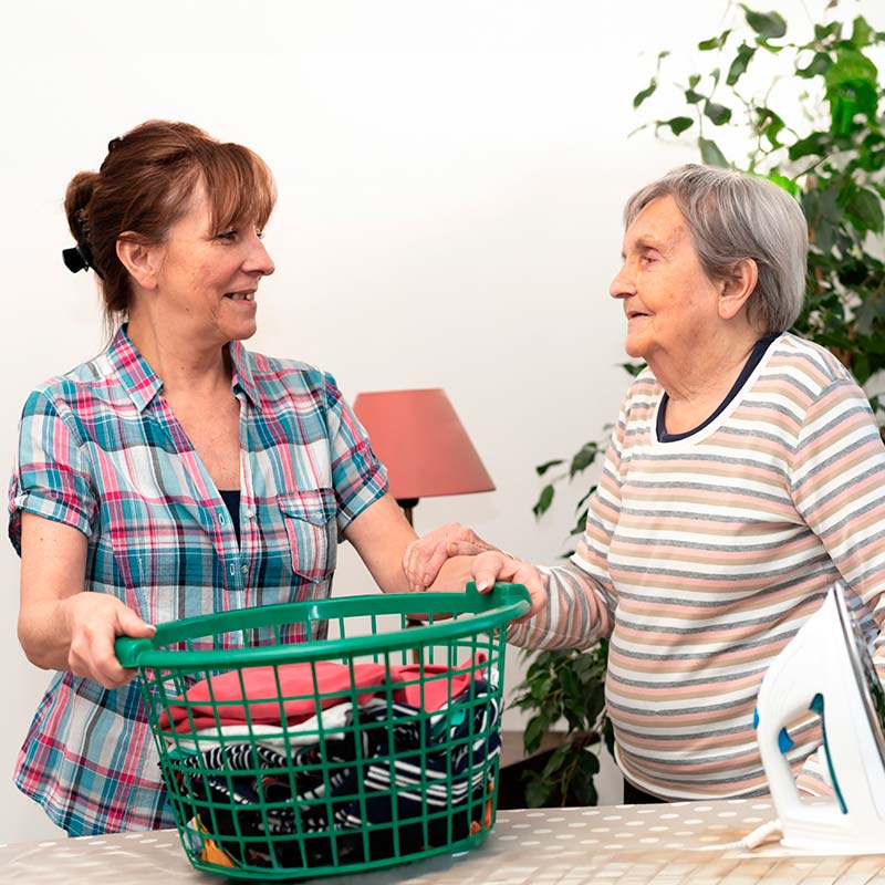 Une aide à domicile aide une personne âgée pour l'entretien du linge